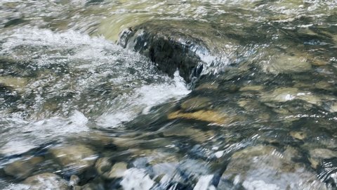 Mountain creek on stone landscape. Closeup clear water stream with foam on rock. Macro shot of tiny river rapid on nature background. Fast stream current with pebbles on bottom. Tiny waterfall outdoor