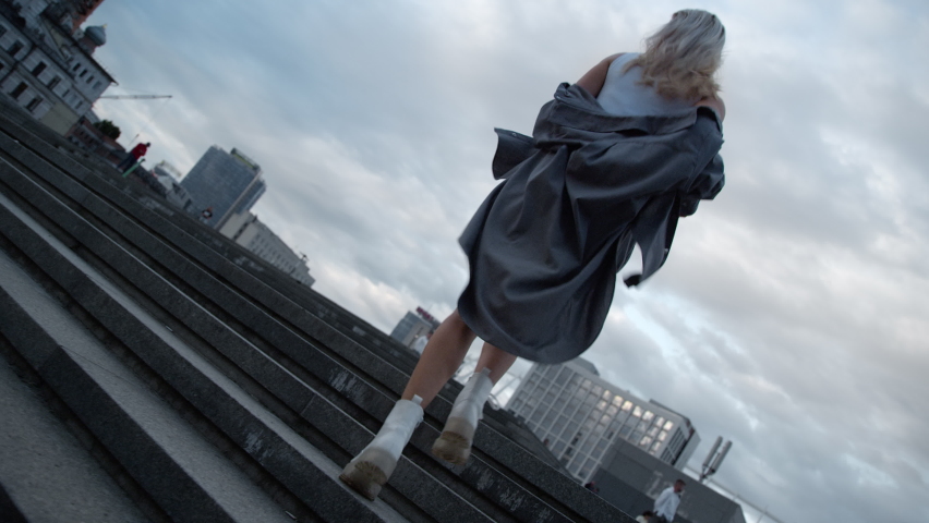Young woman walking stairs at evening town in urban area. Back view female person running in big city landscape in cloud weather. Unknown girl in casual clothes going up stairs. City running concept.