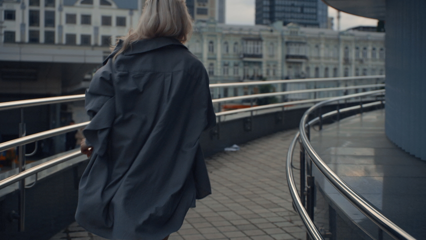 Active girl running away in city background or downtown street outdoors. Back view woman with blonde hair jogging in town. Unknown female runner wearing casual clothes in urban area.acti City concept.