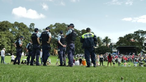 SYDNEY, NSW, AUSTRALIA. DECEMBER 12 2021. A line of Australian police watch anti vaccine rally in a park.