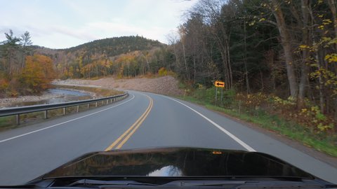Driving black car on Vermont curvy road in Autumn season. Colorful trees and mountain stream by the road side. POV
