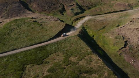 Drone view vehicle driving in mossy highlands in Iceland countryside speeding offroad. Aerial view 4x4 car driving dust road desert countryside with moss hills. Commercial and insurance