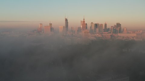 Forwards fly above fog. Panoramic footage of downtown high rise buildings in morning sun light. Revealing cityscape. Warsaw, Poland