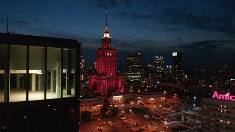 Panoramic view of square and red lit Palace of Culture and Science at night. Down town skyscrapers in background. Warsaw, Poland