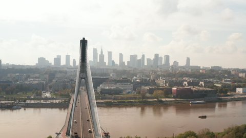 Fly around tall modern cable stayed Swietokrzyski Bridge over Vistula river. Silhouette of downtown skyscrapers panorama. Warsaw, Poland