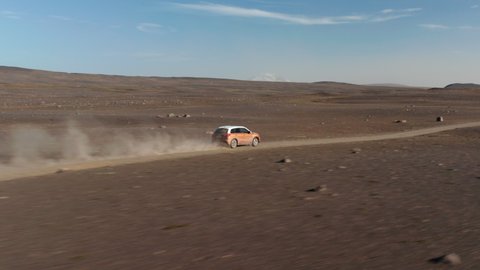Birds eye drone following car speeding along dirt road in Iceland rocky desert stirring up dust cloud. Aerial view 4x4 vehicle driving in icelandic countryside. Freedom concept