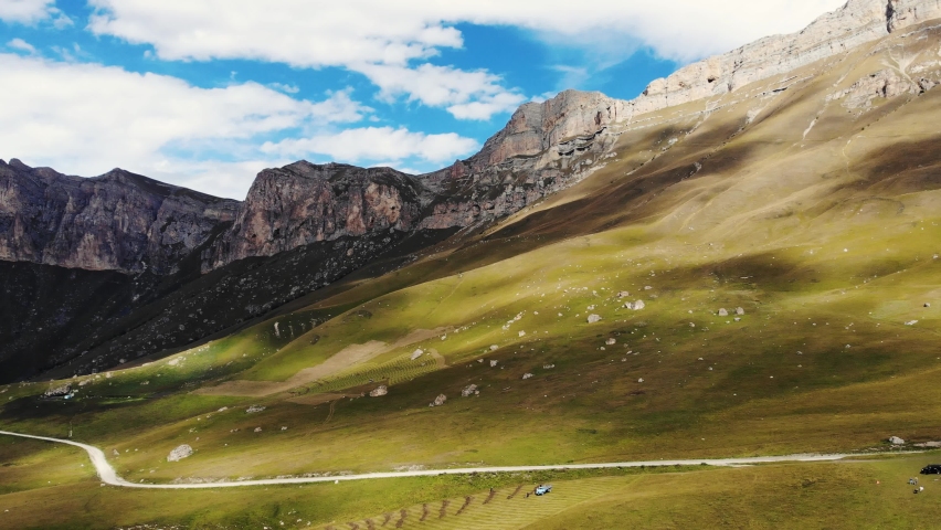 Aerial view of mountain pass, North Caucasus. Range of mountain peaks illuminates the bright sun. Slopes are covered with lush greenery and rocks. The shadow of the clouds runs across the meadows