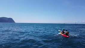 Kayak on sea. Back view. Couple sailing on a boat and paddling. Stock footage. A young couple of tourists on an active water vacation floats on the sea waves in a canoe or kayak. Summer and blue water