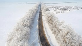 The drone flies over the highway that passes through snowy fields on a sunny day. Bird's eye view. Road conditions in winter. Cinematic aerial shot. Discover the beauty of earth. Filmed in 4k video.