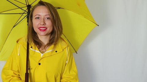 A girl in a yellow raincoat under an umbrella stretches out her hand to the rain. Isolated on white background.