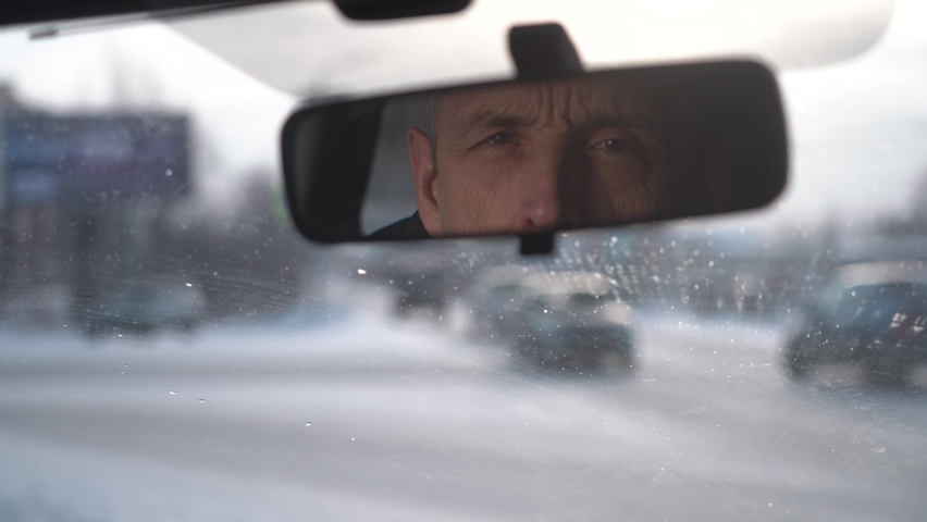 The driver looks at the passenger through the rearview mirror. winter day in the city. experienced driver stands at the crossroads and waits.