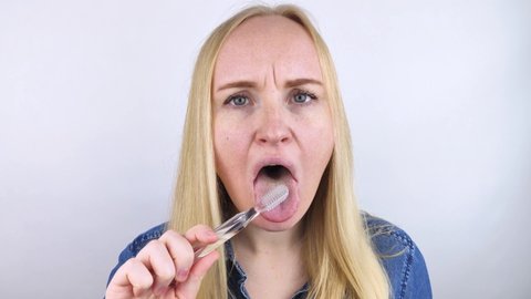 Clean tongue. Close-up of a woman performing antimicrobial hygiene with a special tongue brush. Isolated on white background. A blond female looks into the frame, as if he is looking in a mirror.