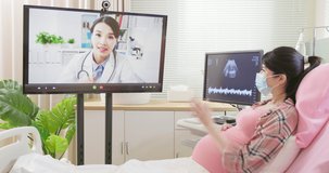 telemedicine concept - asian pregnant woman wearing protective face mask to prevent COVID19 lying in hospital ward has video call with famale doctor by computer screen