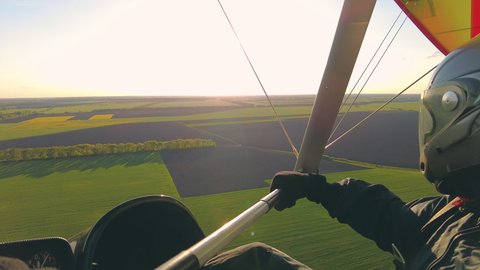 Motorized hang glider flying above field at sunset