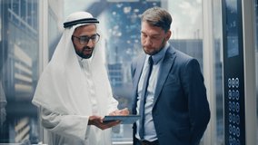 European Businessman Talking with Arab Investment Partner while Riding Glass Elevator to Office in a Modern Business Center. International Corporate Associates Use Tablet Computer in a Lift. - Powered by Shutterstock - Get 15% off with code: PIKWIZARD15