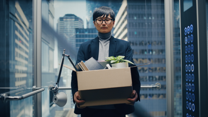 Fired Manager Going Down from Office in a Glass Elevator in Modern Business Center. Sad Specialist Laid Off, Feeling Depressed and Devastated, Holding Office Accessories and a Plant in a Cardboard Box Royalty-Free Stock Footage #1083972244