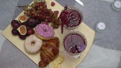 Outdoor picnic in the rain. Two glasses with red wine, mulled wine or juice. The drops are falling in rainy weather. Croissant, donuts, figs and grapes are fruits. Romantic date outside.