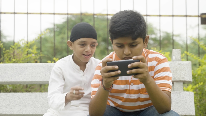 Multiethnic kids playing video game on mobile phone at park - concept of technology, smartphone addiction, friendship and leisure activities
