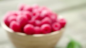 Fresh ripe red raspberries with leaves in a bowl on rustic old wooden table in 4K VIDEO. Organic farming, healthy food, BIO viands, back to nature concept.