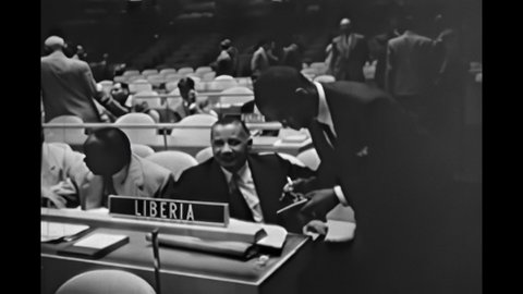 1950s: Men speaking over table. Security officer admitting woman through gate. Men sitting on patio, speaking. Man taking notes. Man walking into building. Headquarters of the United Nations.