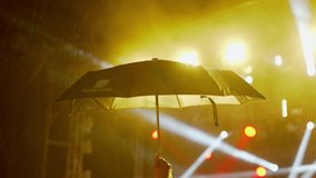 Happy people watch an amazing music concert under umbrellas in the rain. Merry fans jump and raise their hands up. Multicolored light at a music festival.  - Powered by Shutterstock - Get 15% off with code: PIKWIZARD15