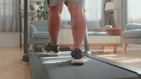 Back View Of Legs Of Asian Fat Man Wearing No T-Shirt And Training On Walking Treadmill At Home
