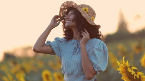 Portrait of beautiful young asian woman posing in field with sunflowers and enjoying nature. Woman smells flowers against background of nature and field of sunflowers. 