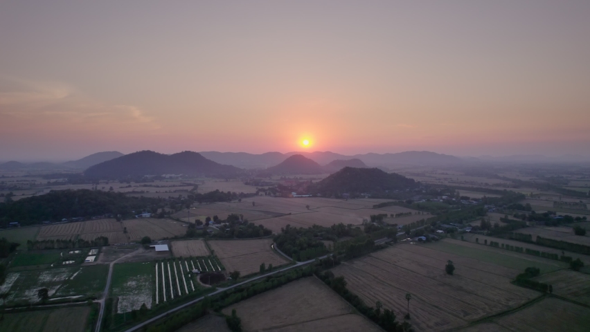 Aerial view of Colorful sunset over mountain and harvested paddy fields in farmland at countryside