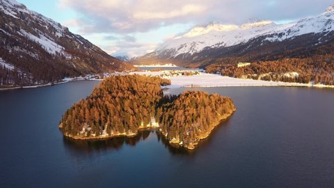 Aerial drone footage of the sunset over the Silsersee lake in winter in the Engadine valley in Sils Maria village in Canton Graubunden in the Swiss alps. Shot with a backward tilt up motion