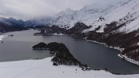 Aerial drone footage of the Sils Segl Maria village by the Silsersee lake in winter in the Engadine valley in Canton Graubunden in the Swiss alps. Shot with a rotation motion
