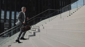 Side view of caucasian aged man in stylish suit and eyeglasses walking up on stairs with suitcase in hands. Busy male emloyer in hurry. - Powered by Shutterstock - Get 15% off with code: PIKWIZARD15