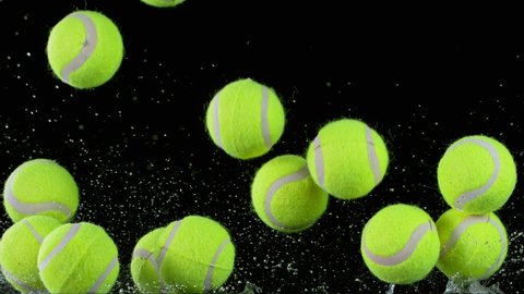 Super slow motion of falling tennis balls on water surface, black background. Filmed on high speed cinematic camera.