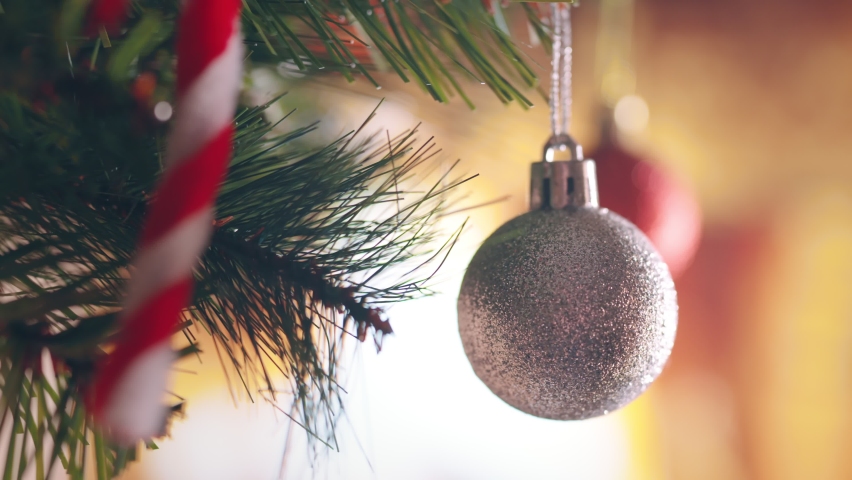 B roll - Close-up hand of woman playing Christmas balls on the background of festive lights at home.