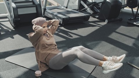 High angle shot of Muslim woman in hijab and sportswear performing v-sits exercise on mat while having abs workout in gym