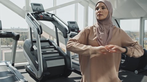 Muslim woman in hijab and sportswear doing torso rotations while warming up before workout in gym
