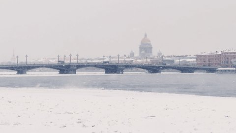 Slow motion footage of winter view of St. Petersburg at snow storm, frozen Neva river, steam over city, Isaac cathedral, car traffic on Blagoveshenskiy bridge, Palace drawbridge, panoramic view