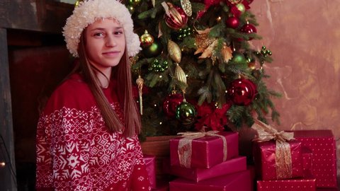 Young woman in santa hat sit near Christmas tree with presents