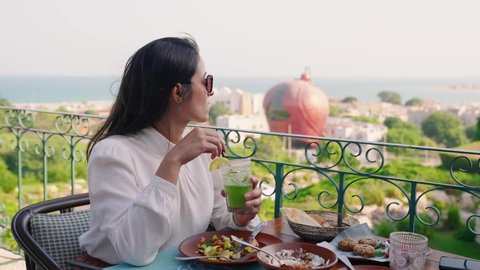  Woman tourist driking lemonade with Katara Cultural village view in Doha Qatar
