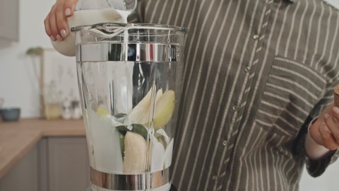 Close up shot of woman pouring milk in blender with fresh fruit in it while making smoothie at home