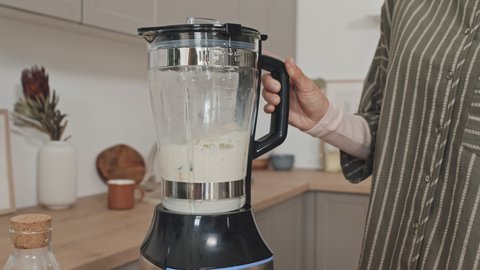 Close up shot of unrecognizable woman holding blender with fresh smoothie in it while standing in kitchen at home