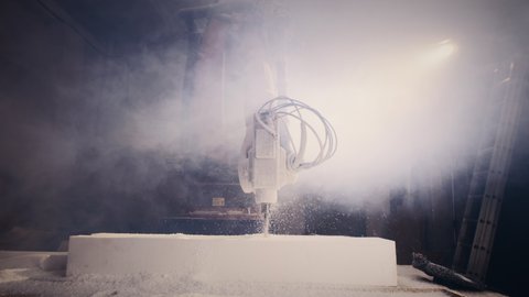 Modern robotic arm milling machine cutting block of polymer in cloud of smoke in professional workshop