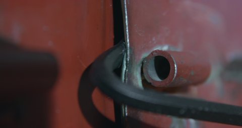 Thief breaks down professionally thick dark red steel door OF storage with help of grey metal pry bar and opens entry closeup