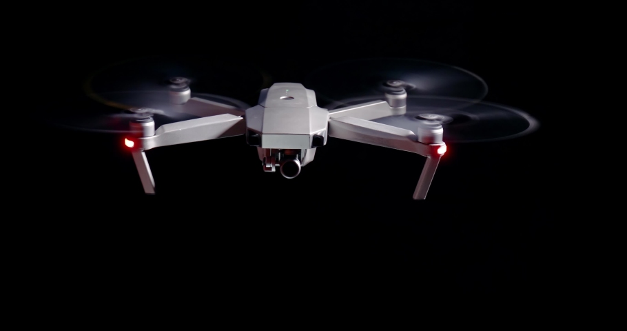 Drone flying hovering agains dark black background, isolated lighting