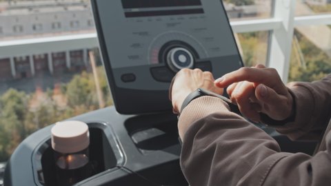 Close up shot of woman standing on treadmill in gym and setting fitness tracker on her hand