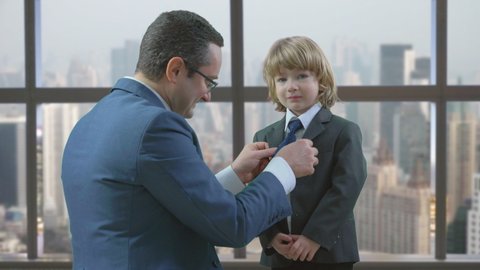 Man arrange tie and suit of little blonde hair child, father and son team, office window pcity panorama