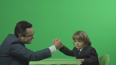 Father and son with suit and tie make arm wrestling, green background