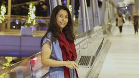 Smiling asian woman looking camera. She searching information, writing plans job for the next year on laptop while standing in city at Christmas night and Decoration light on background.     
