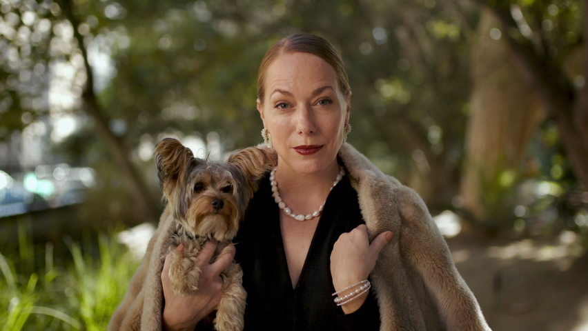 Rich mature woman with her pet dog outdoors. High society female wearing a fur jacket and holding her pet and looking at camera. Royalty-Free Stock Footage #1084024477