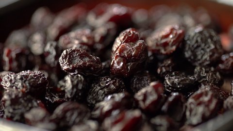 Close up macro view of Black dry grape raisins, moving food texture. Concept of healthy and organic food. Dried fruits snacks on red bowl.