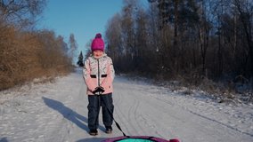 Cute child walking with snow tube at winter woods outdoors. Young female person school age holding sledding in hands and having fun. Youth people and winter leisure activity and sports concept